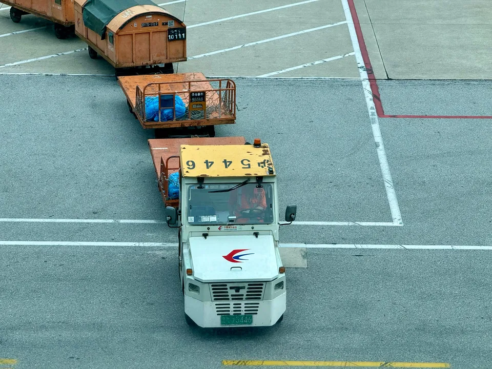 Tractor de rampa arrastrando un tren de carretillas con contenedores de carga sobre la plataforma de estacionamiento de un aeropuerto.